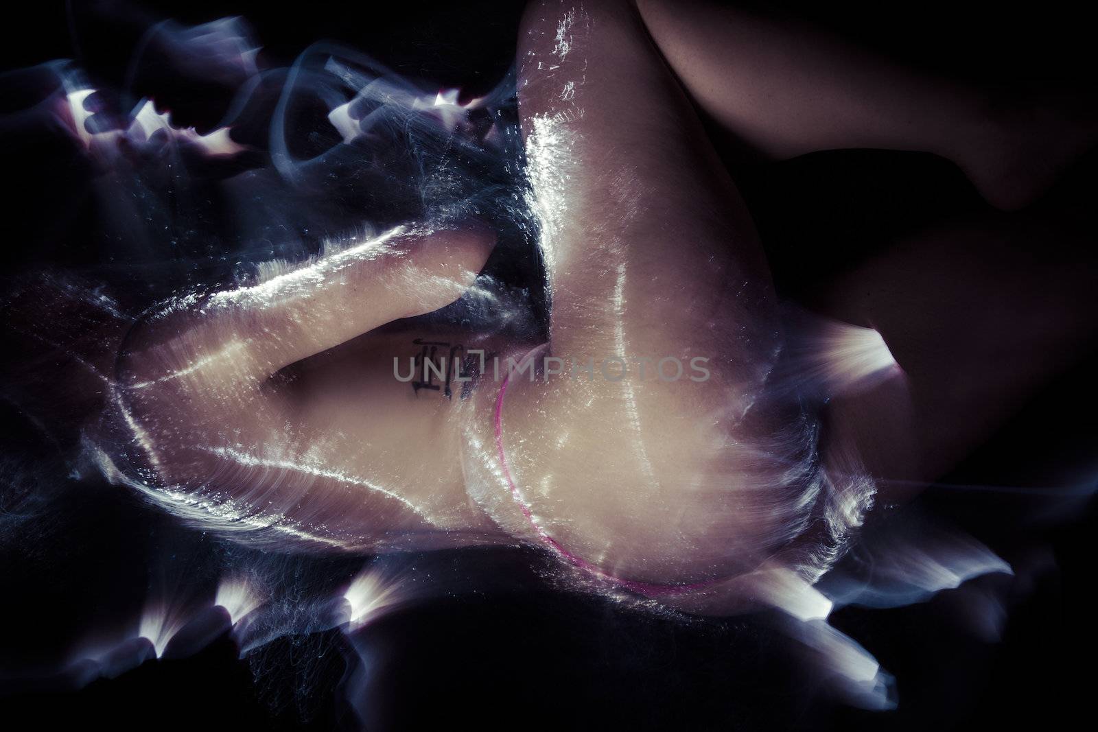 Artistic nude, tattoed woman lying with fiber optics and light effects on her skin