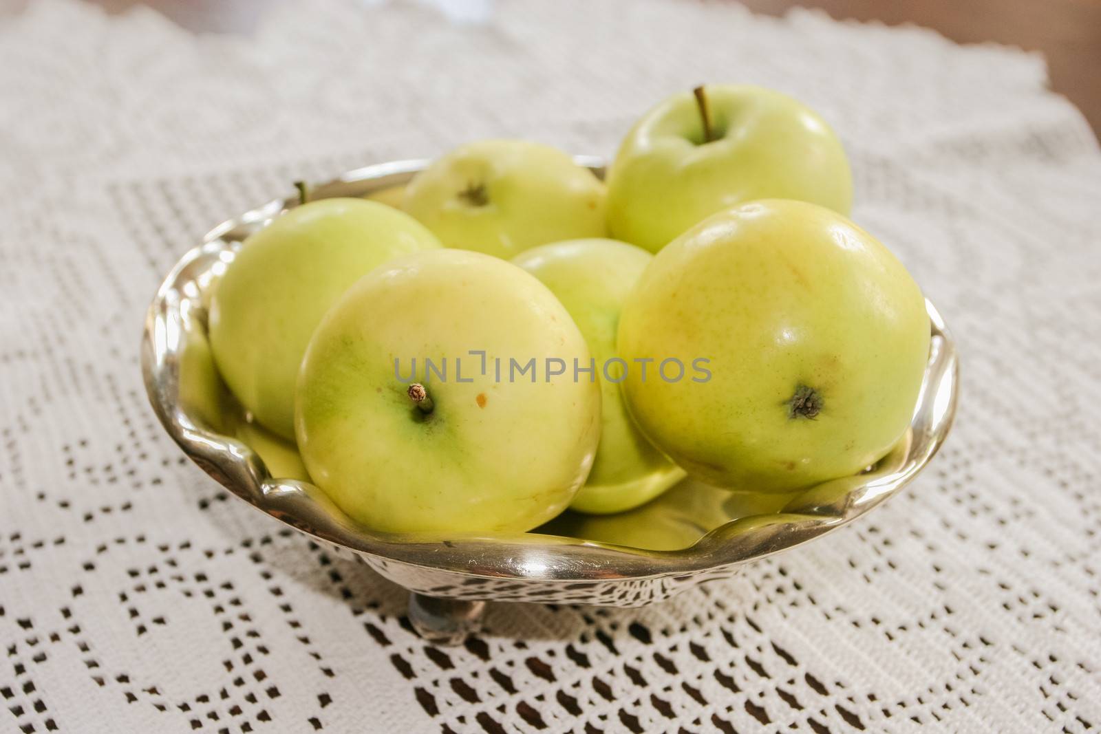 Freshly picked green apples in a metal bowl on a table.