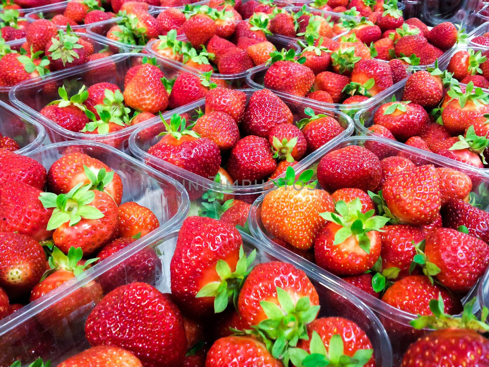 Strawberries with green weed in plastic containers at marketplace