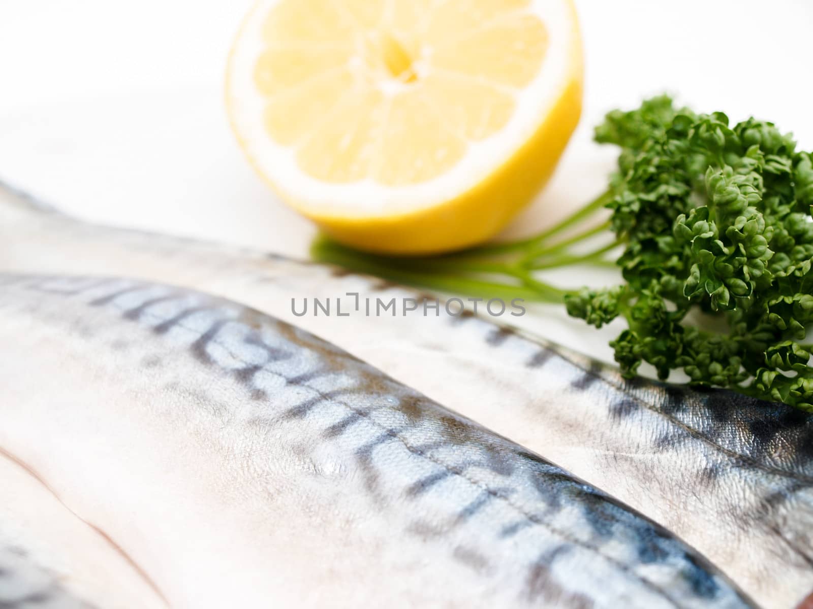 Closeup of raw mackerel filet, half a lemon and parsley on the side