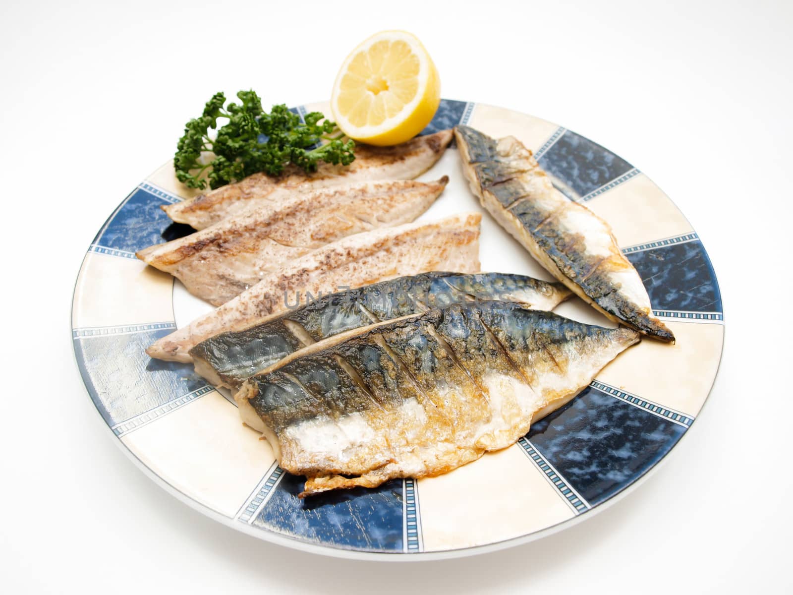 Fried filet of mackerel fish on colored plate with half a lemon and parsley