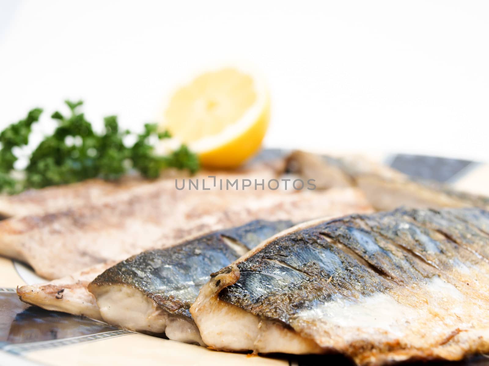 Fried filet of mackerel fish on colored plate with half a lemon and parsley