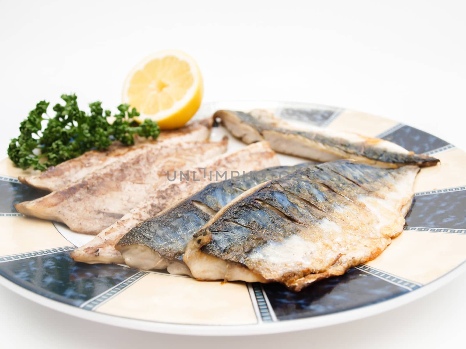 Fried filet of mackerel fish on colored plate with half a lemon and parsley