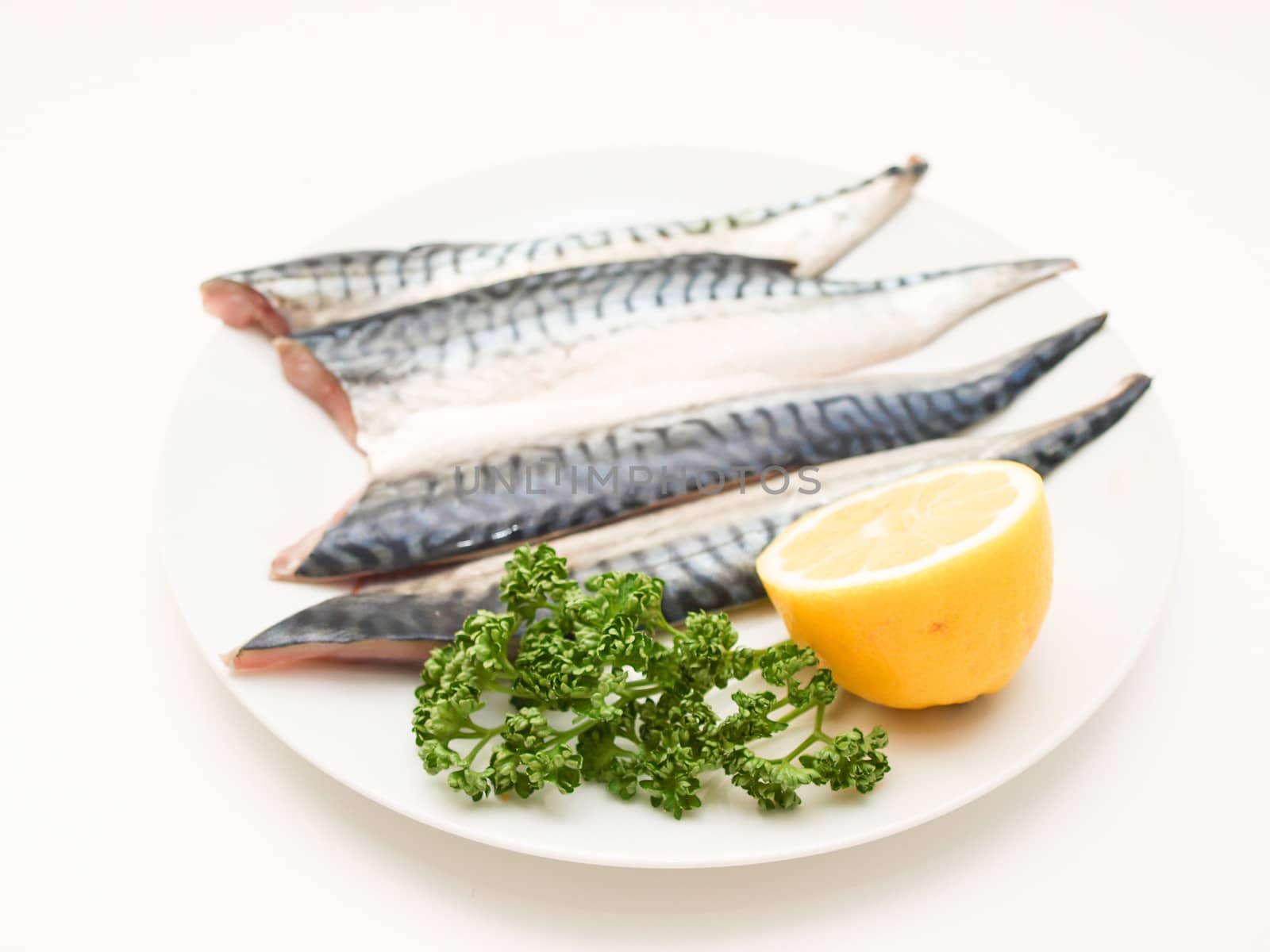 Raw mackerel fish filet with half a lemon and parsley on white plate