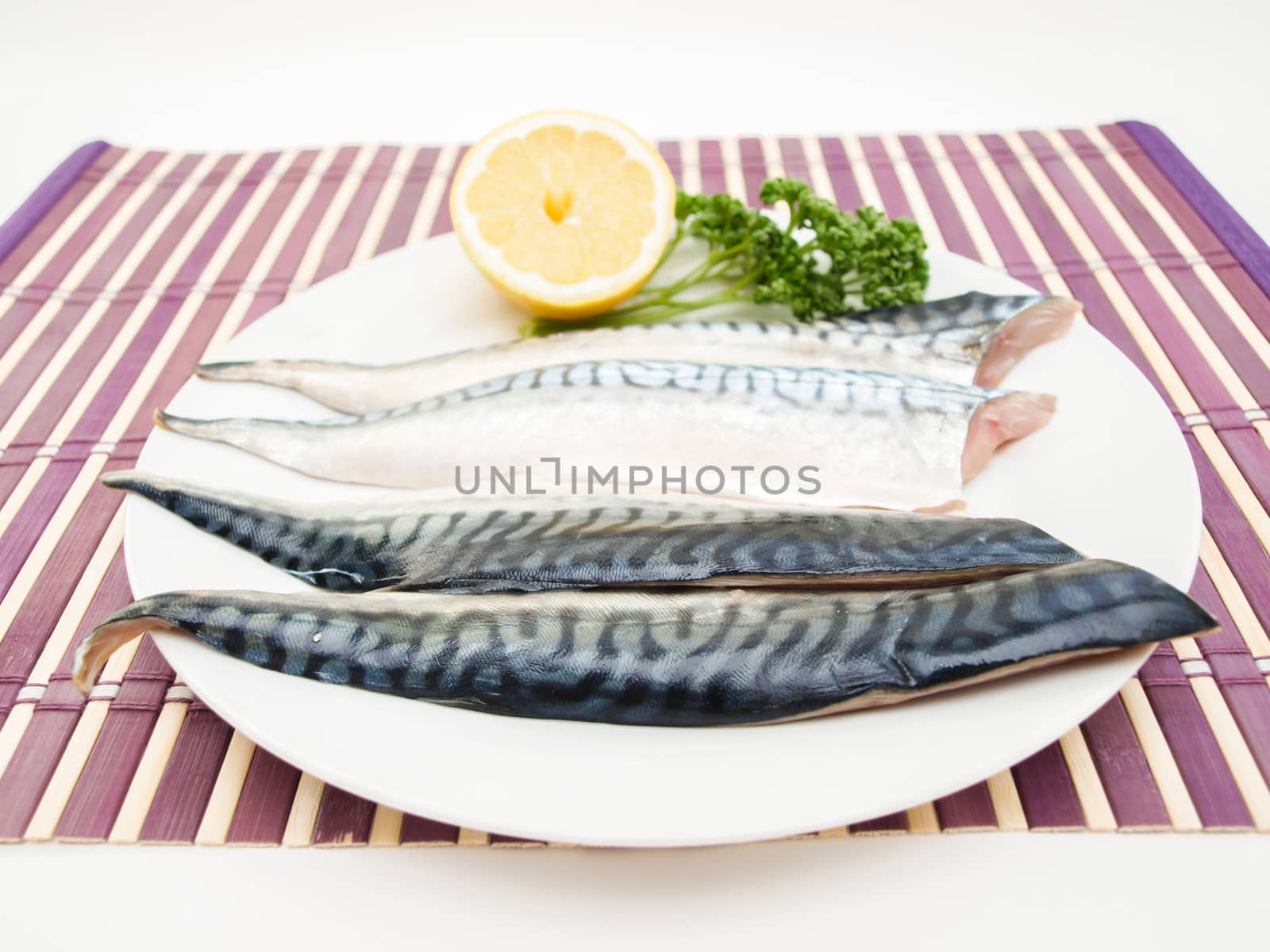 Raw mackerel fish filet with half a lemon and parsley on white plate on purple wooden table cover