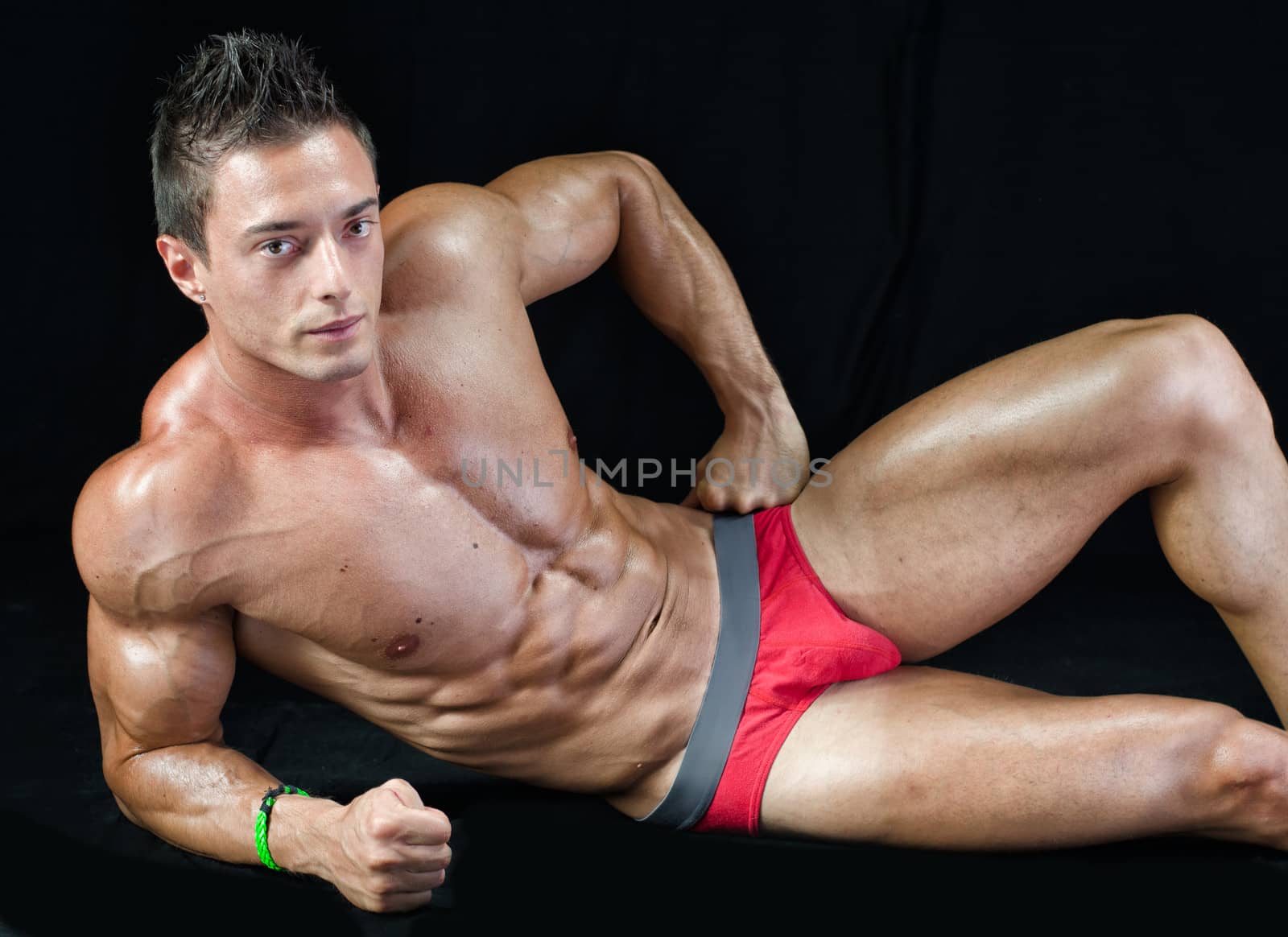 Handsome young bodybuilder laying down on the floor, showing ripped abs, muscular  pecs, arms and legs