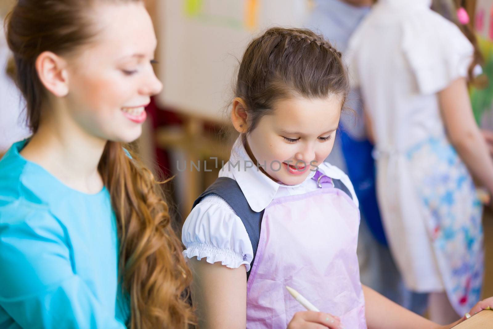 Little girl painting with teacher at kindergarten