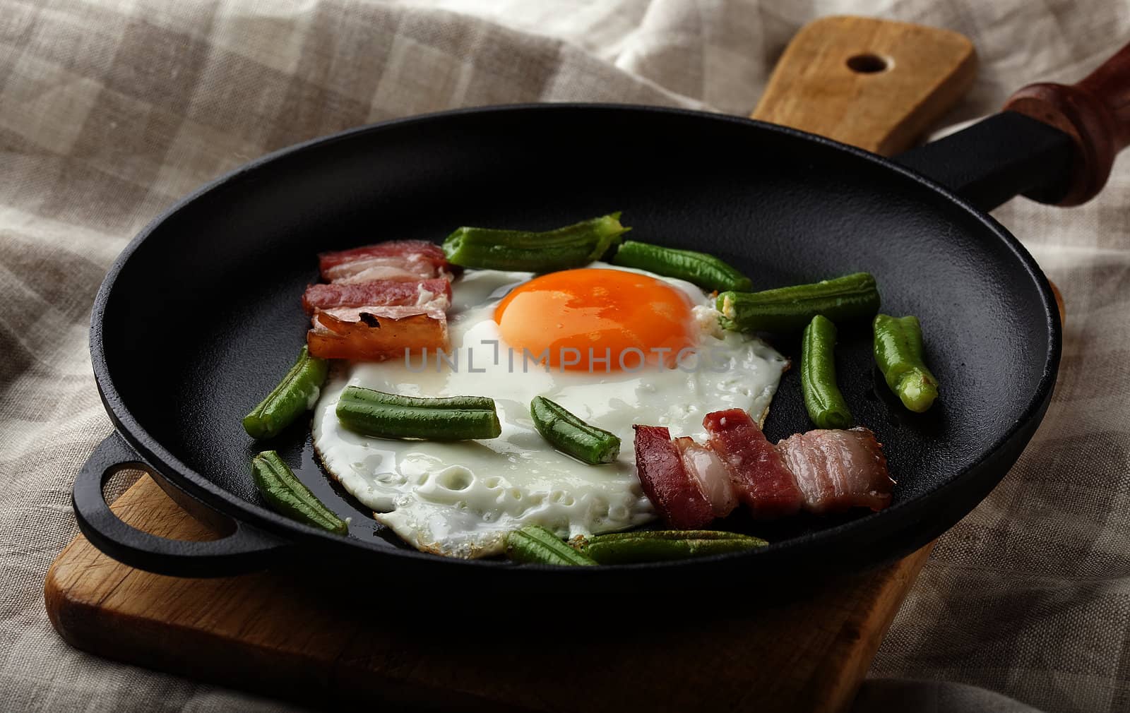 Fried egg with bacon and string bean on the black pan