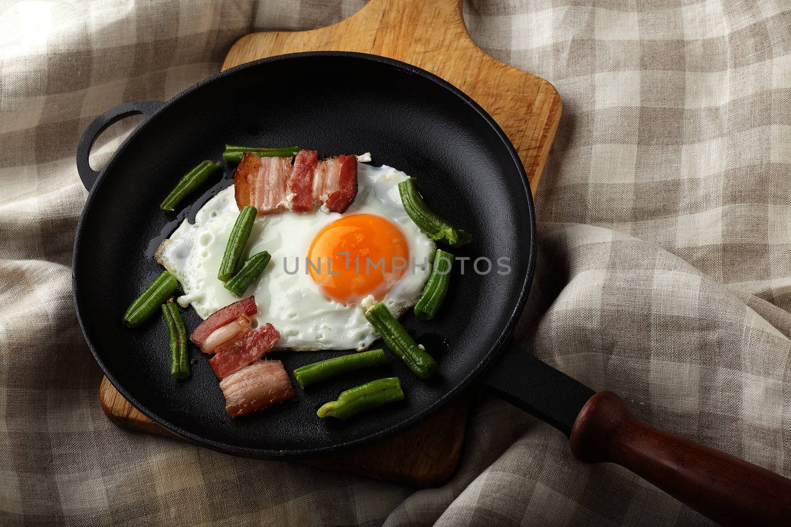 Fried egg with bacon and string bean on the black pan