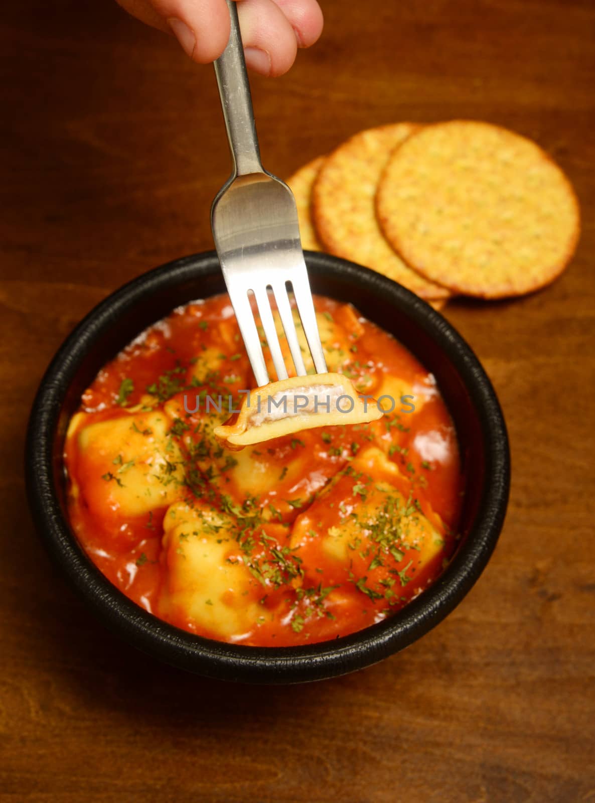 hand holding ravioli on fork and wood background by ftlaudgirl