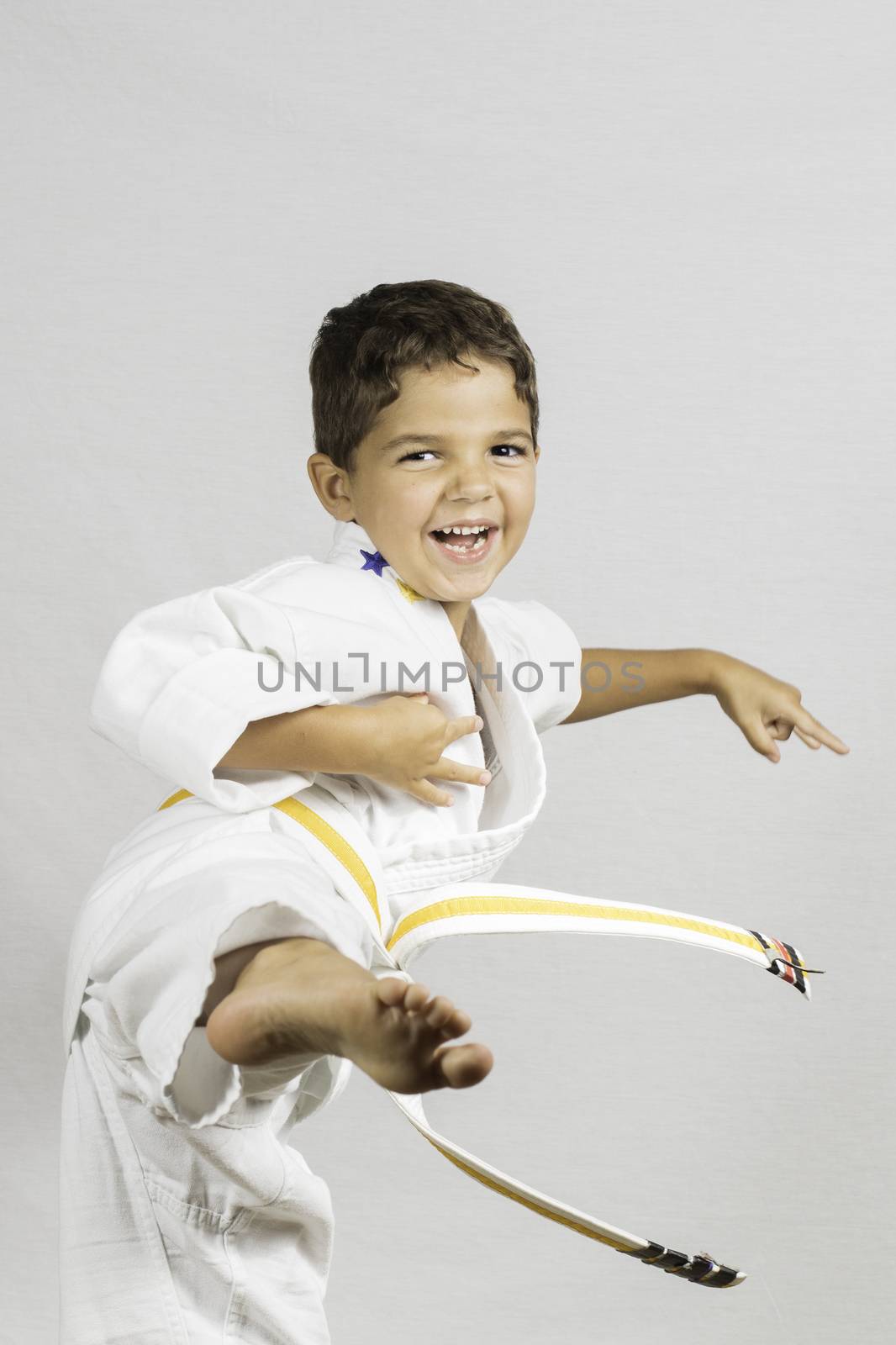 A young boy jumping and kicking dressed in a karate uniform.