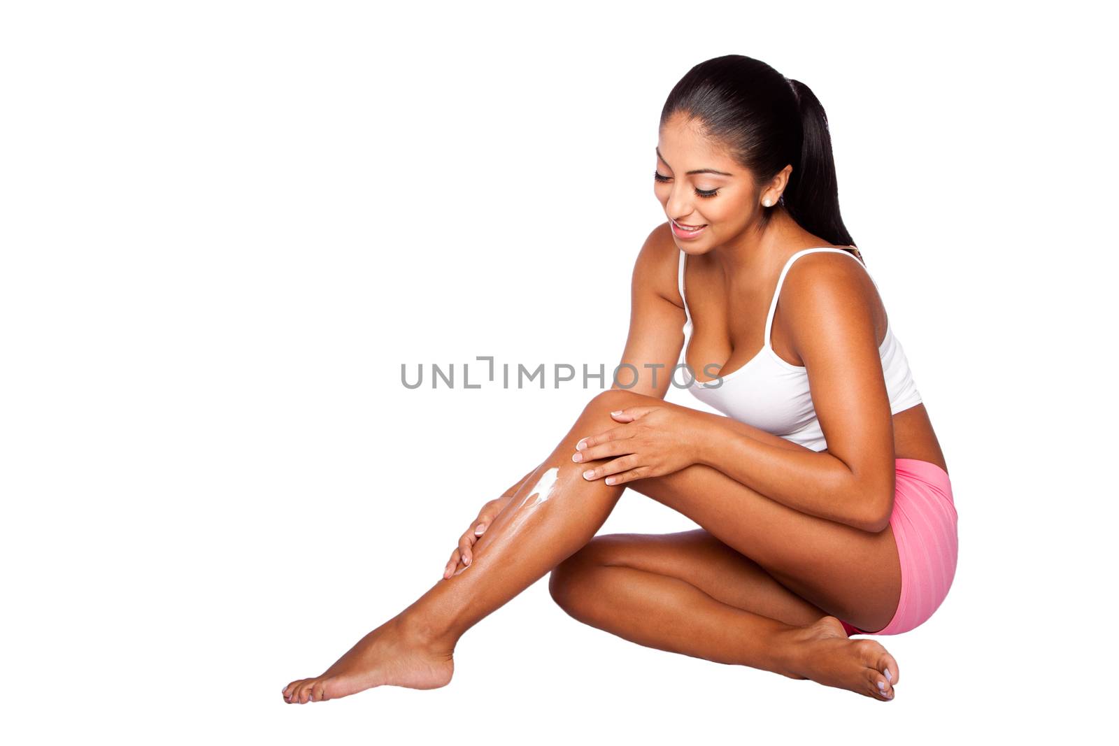Beautiful happy smiling woman applying exfoliating moisturizing lotion cream on leg, bodycare skincare concept.