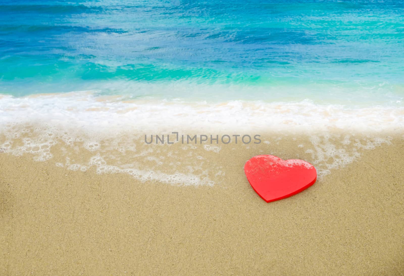 Red Heart shape on sandy beach by ocean