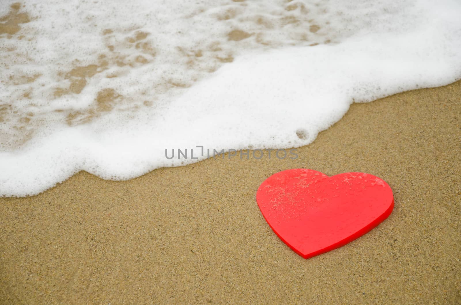 Red Heart shape on sandy beach by ocean's wave