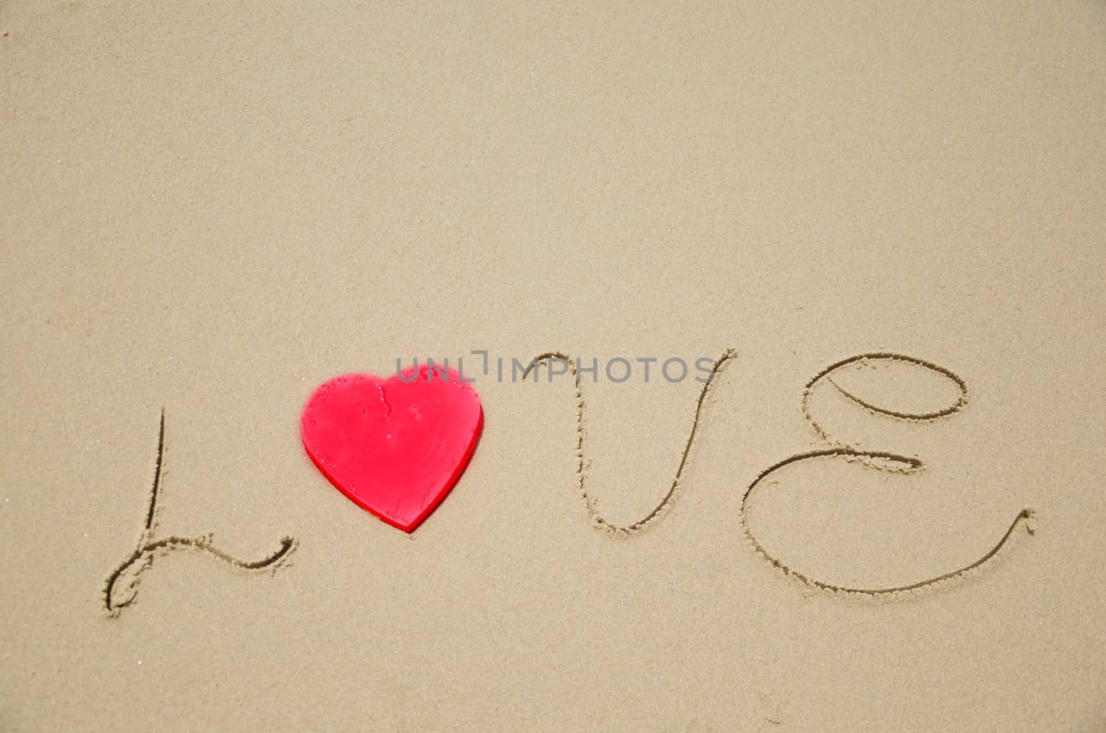 Sign "Love" with red heart shape on the sandy beach