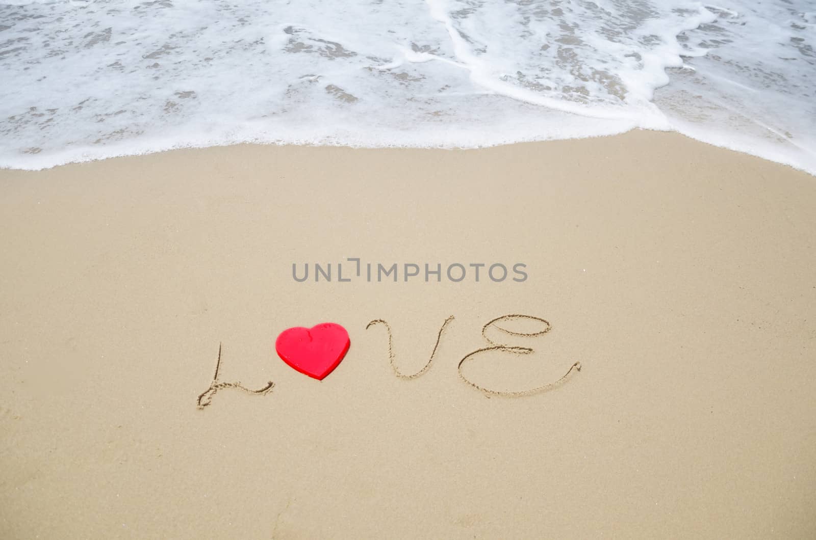 Word "Love" with red heart shape on the sandy beach