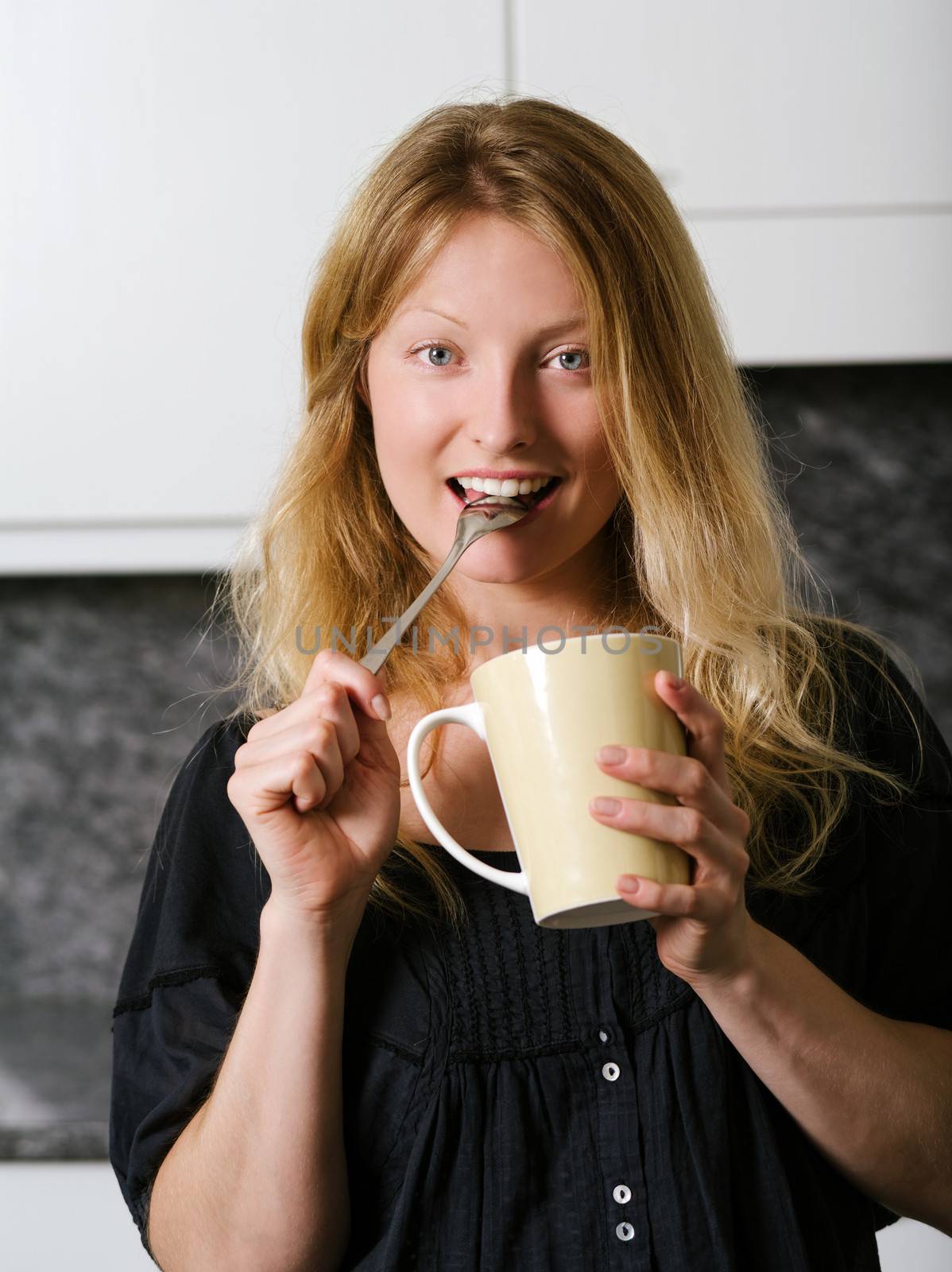 Photo of a beautiful blond holding a large coffee and a spoon in her mouth.
