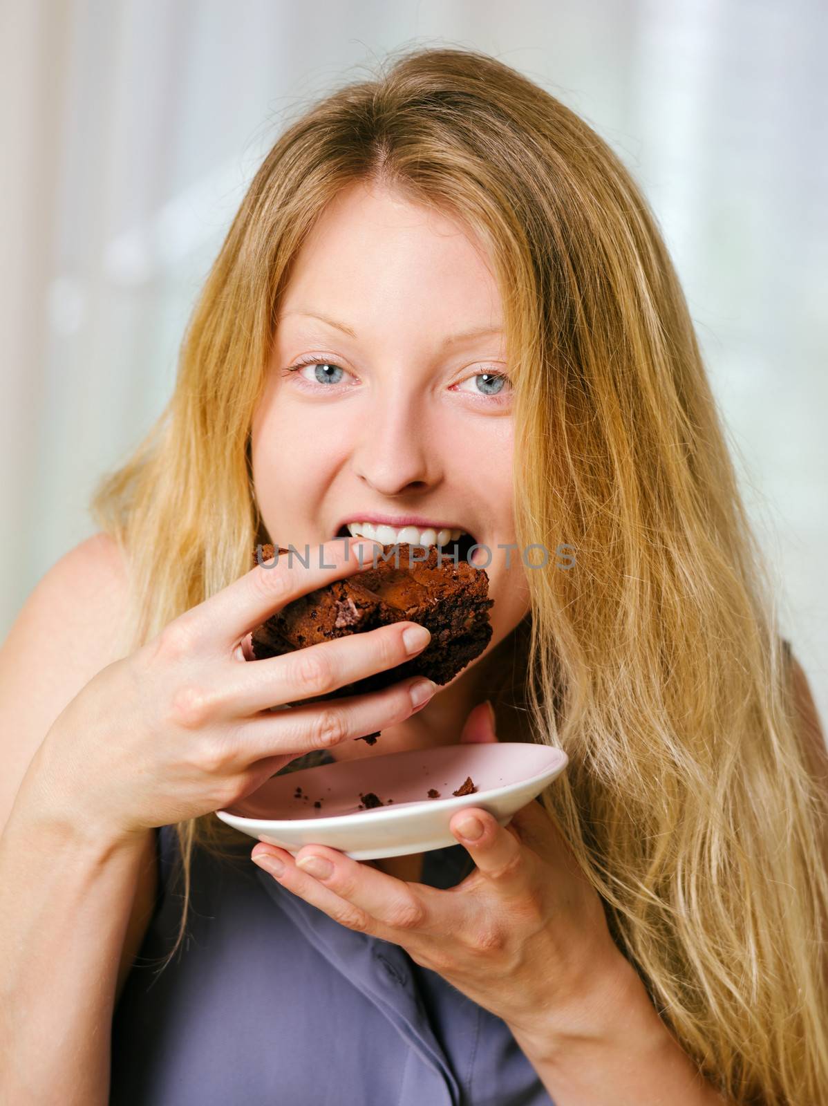 Photo of a beautiful blond woman in her early thirties with log blond hair eating a large piece of brownie or cake.