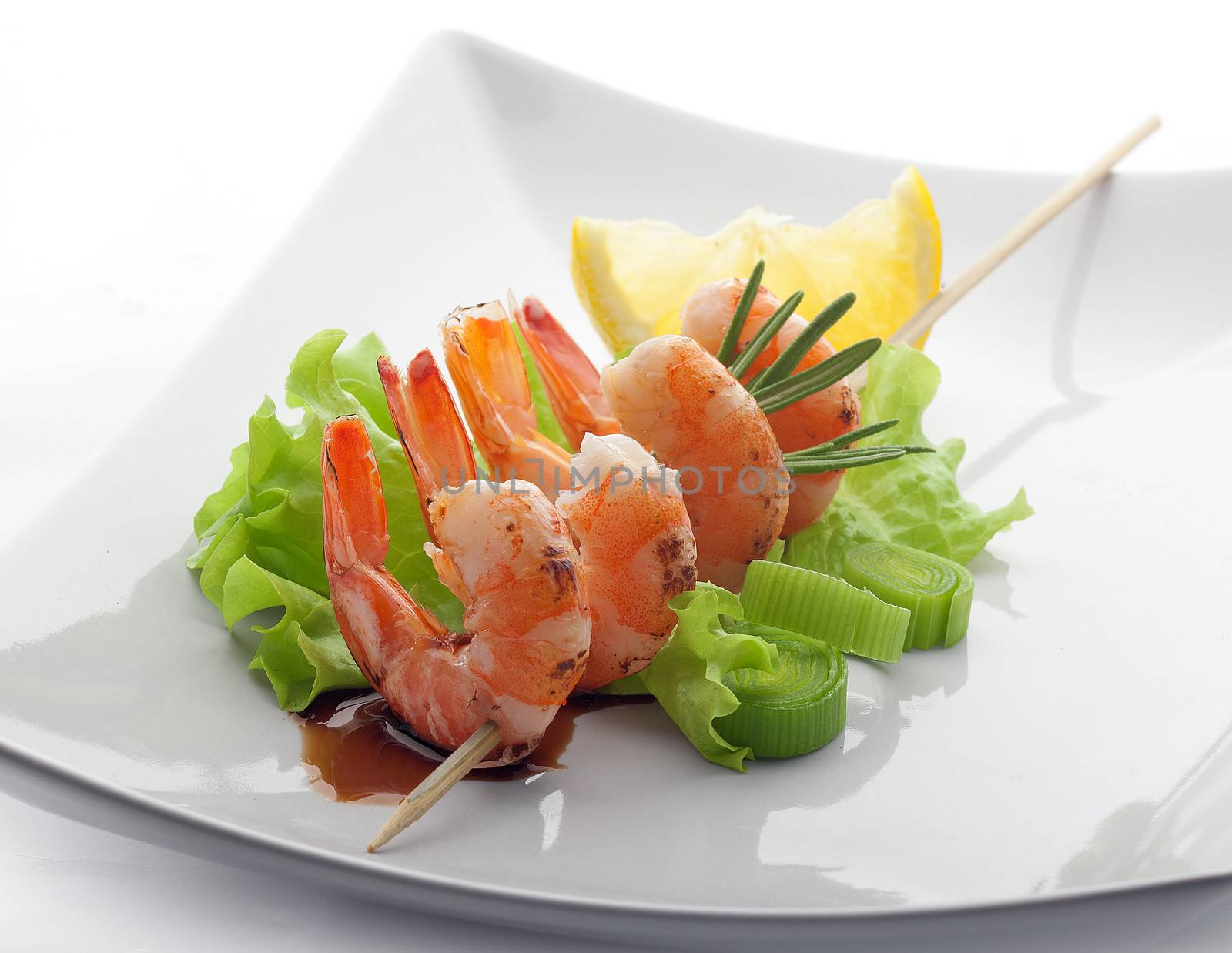 Four roasted shrimp's tails on the scewer with lettuce, lemon and soy sauce