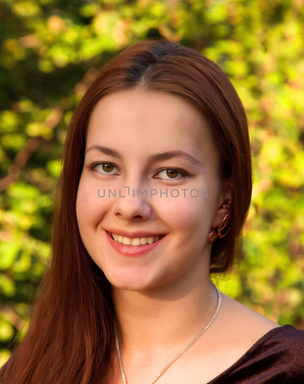 Young happy girl on a background of green foliage. Portrait