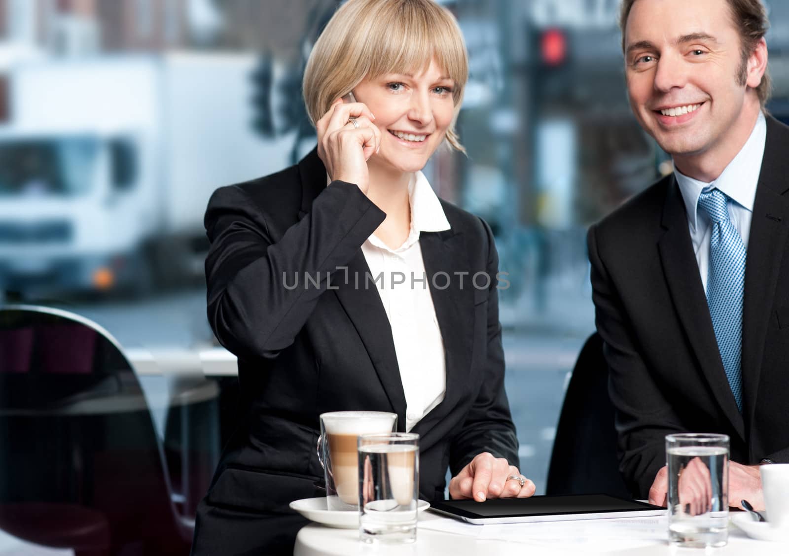 Business partners enjoying coffee while discussing work in open-air restaurant.