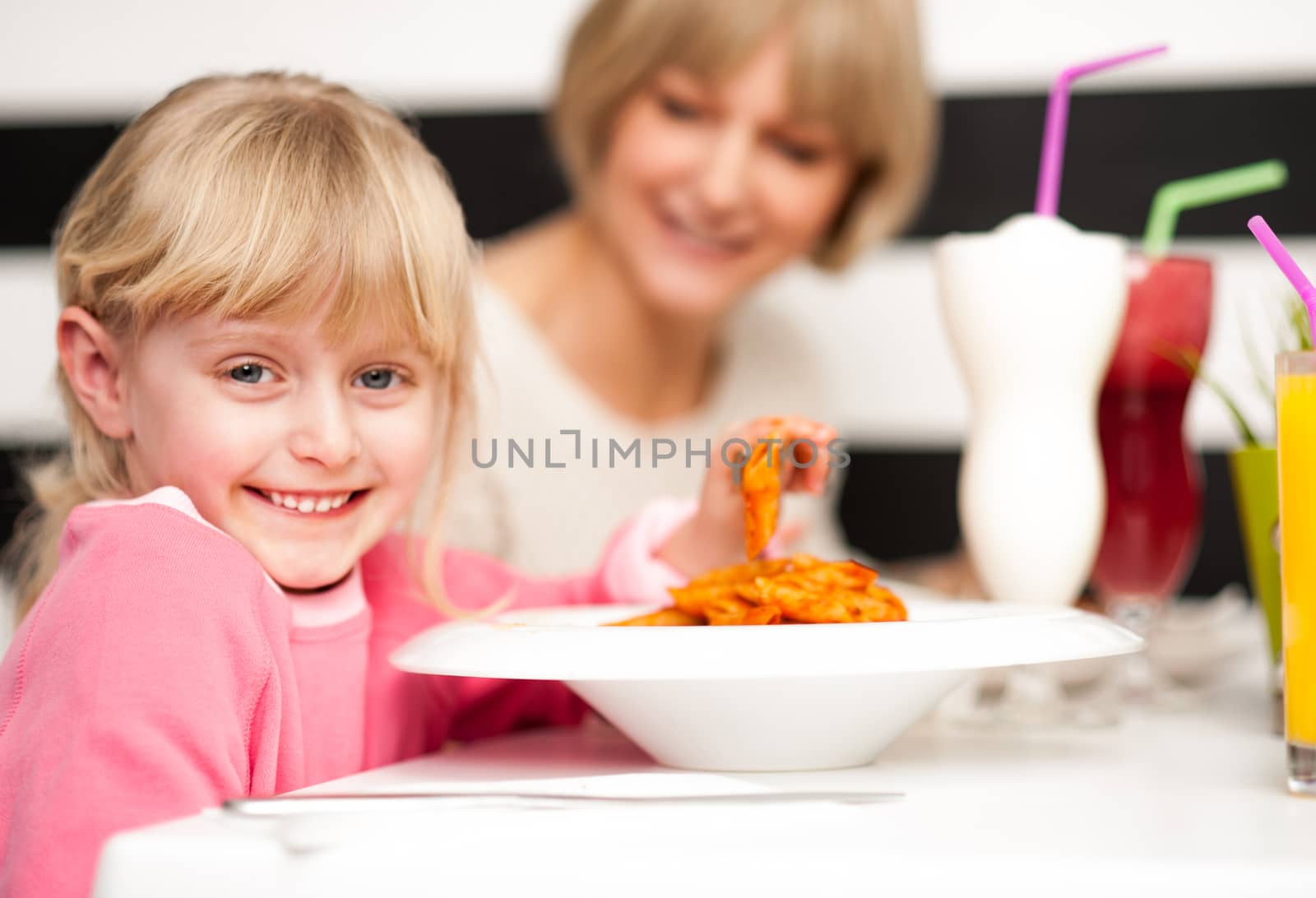 Cute girl kid enjoying meal and juice in restaurant with her mother.