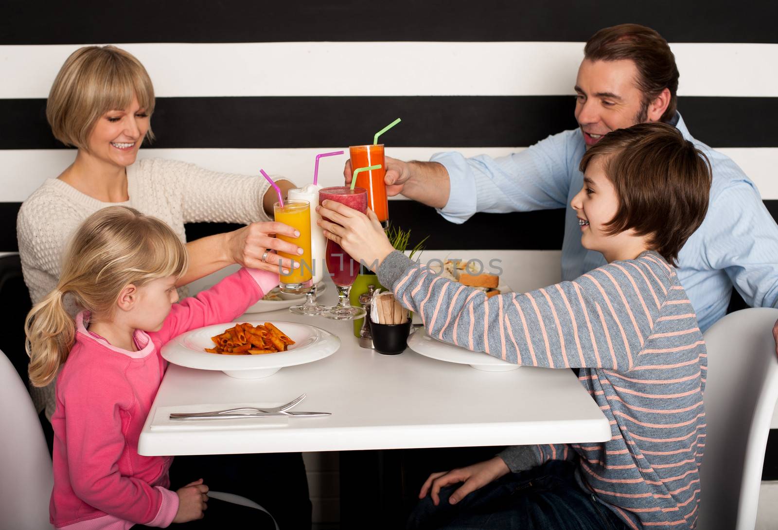 Family toasting smoothies in restaurant by stockyimages