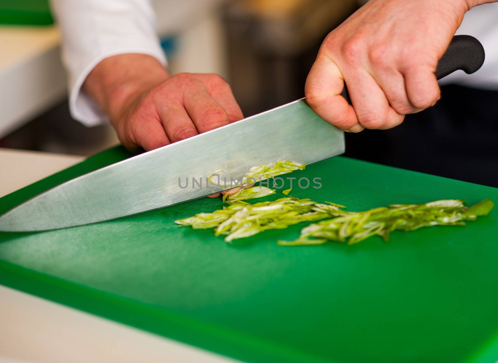 Chef chopping leek over green carving board.