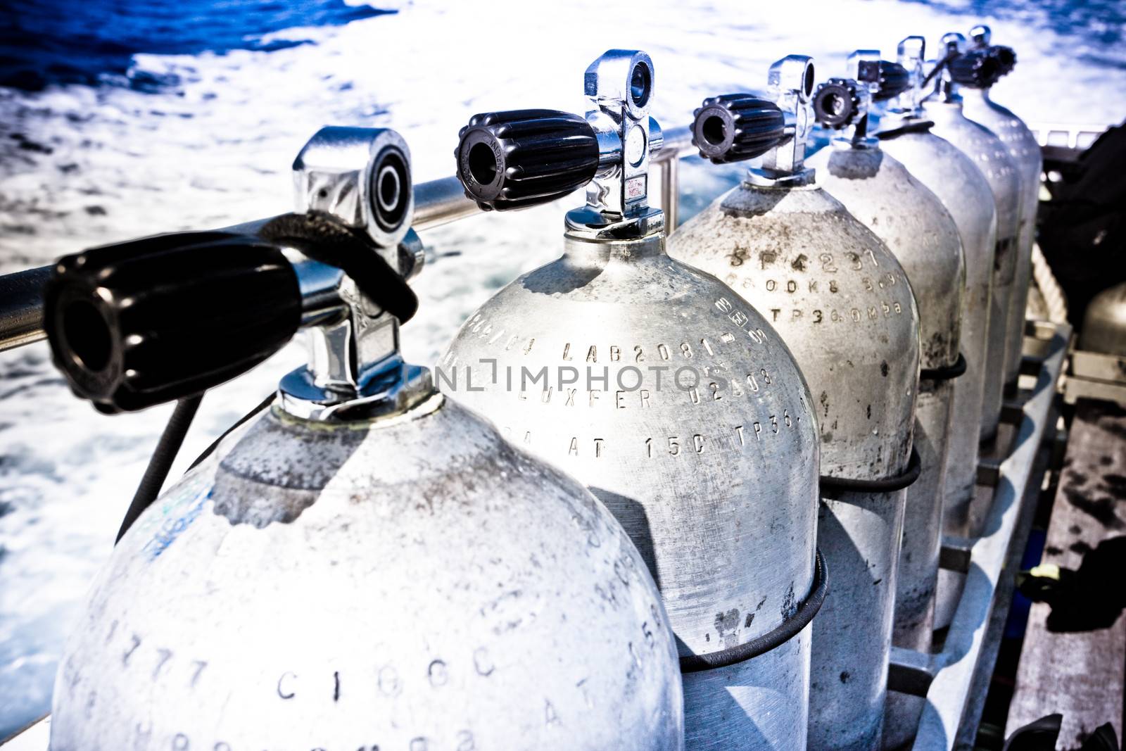 Rows of air tanks with attached valves for scuba diving lined up on the deck of a dive ship in mid ocean