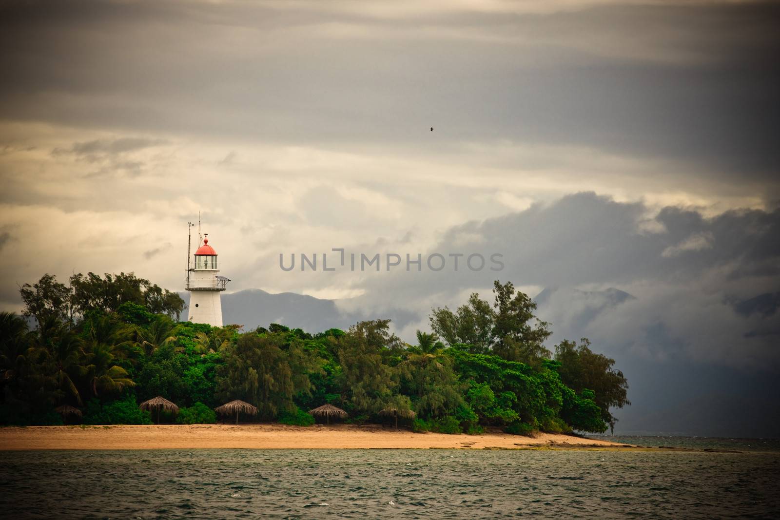 Lighthouse to warn ships and act as a navigation beacon on the Australian coast on a sandy peninsula with lush tropical vegetation under a cloudy sky