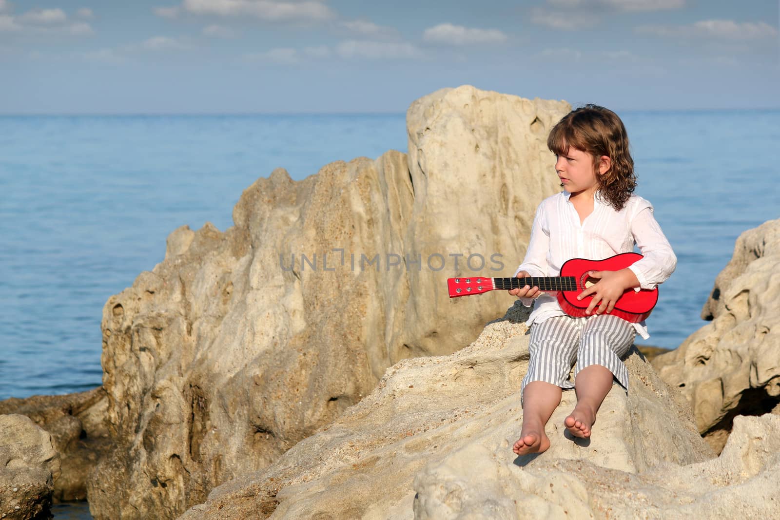 little girl with guitar sitting on rock