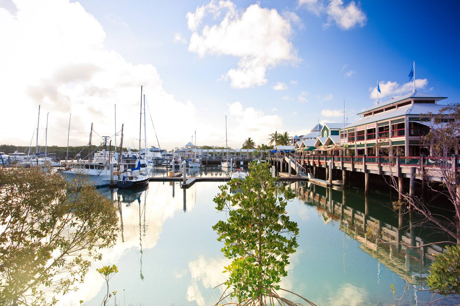 Pleasure yachts moored in a calm marina with the waterfront buildings and clouds reflected on the water