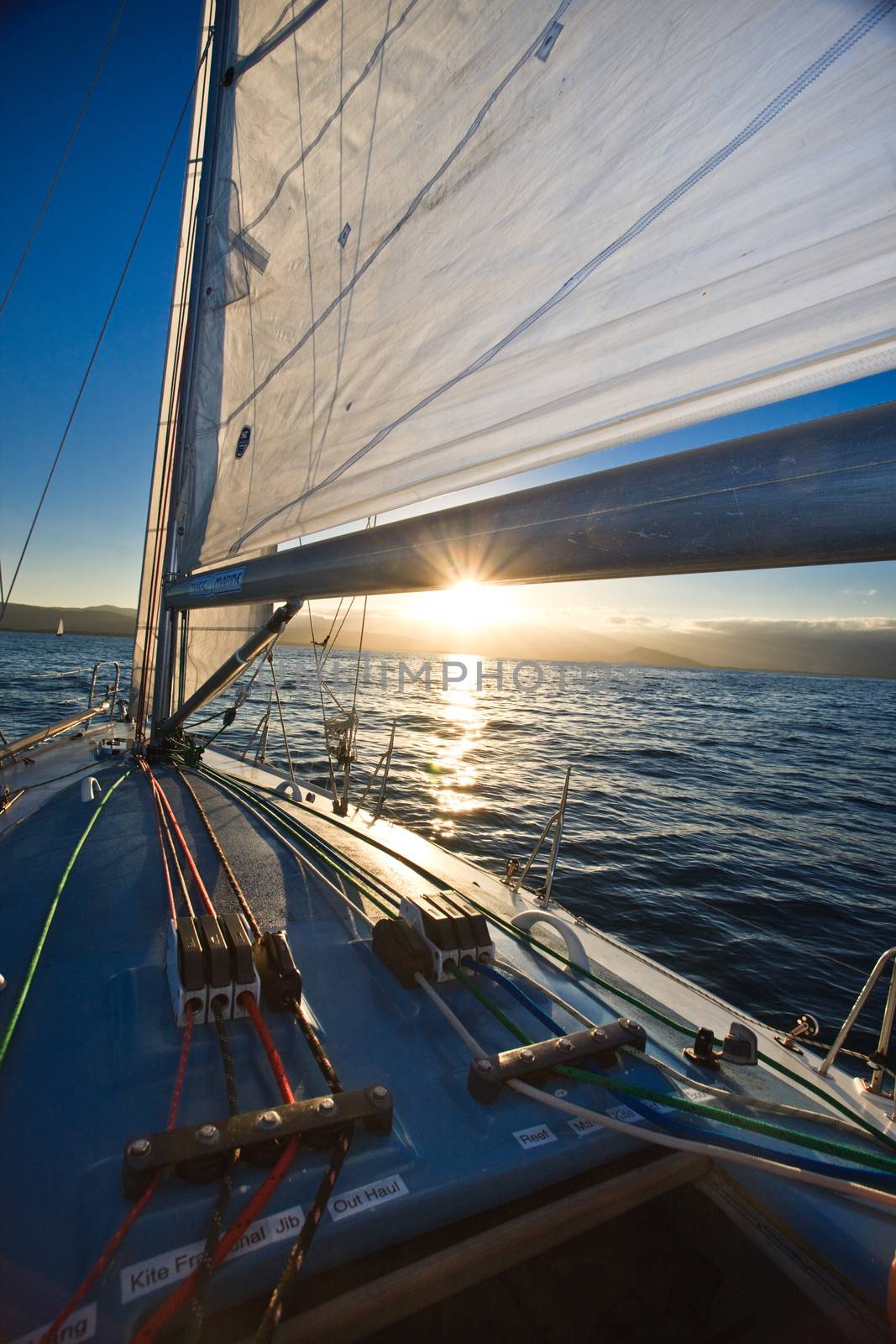 Sunset from the deck of a yacht with the sun just dipping towards the horizon under the sail of the boat