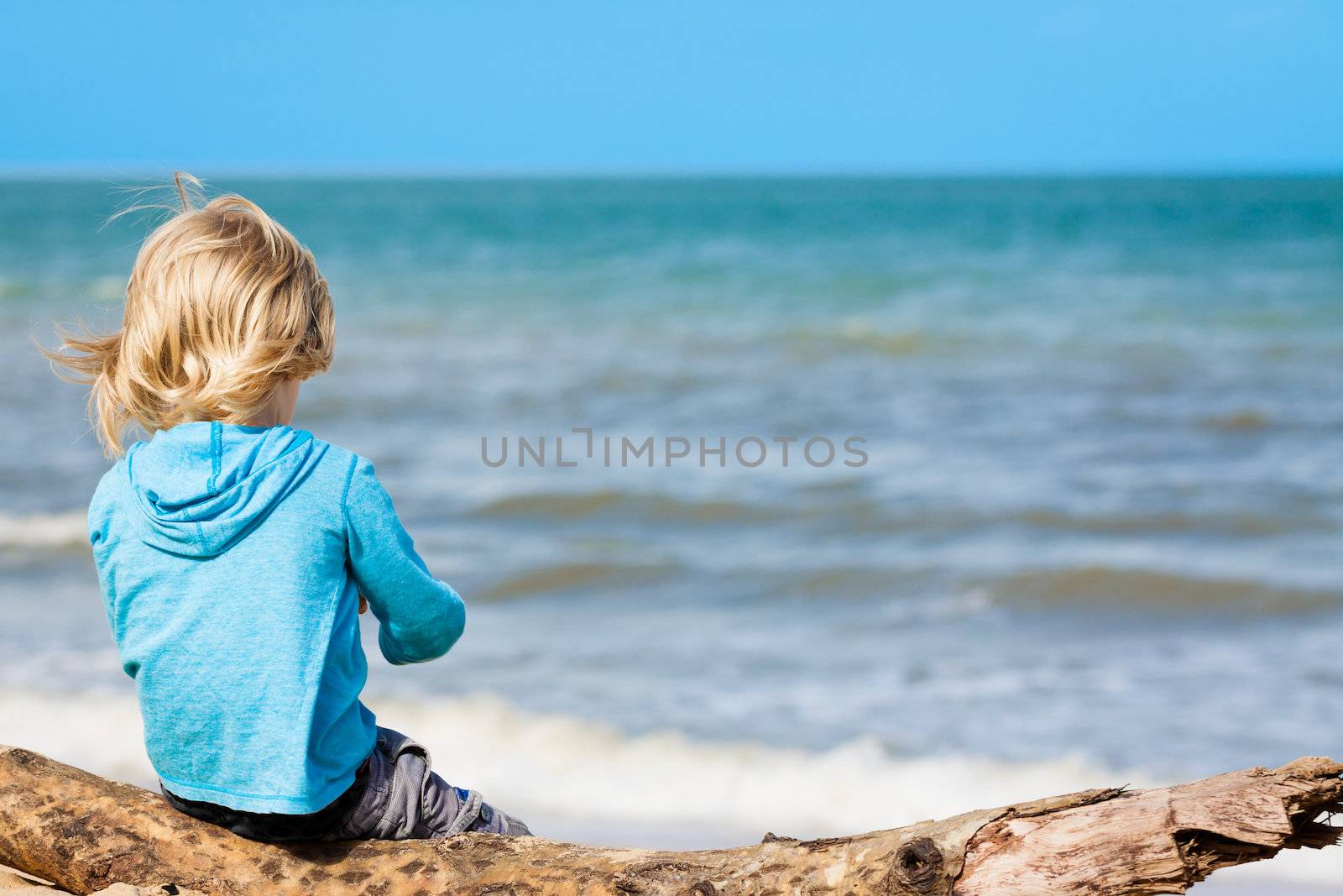 A young carefree child sitting on a log at the beach.