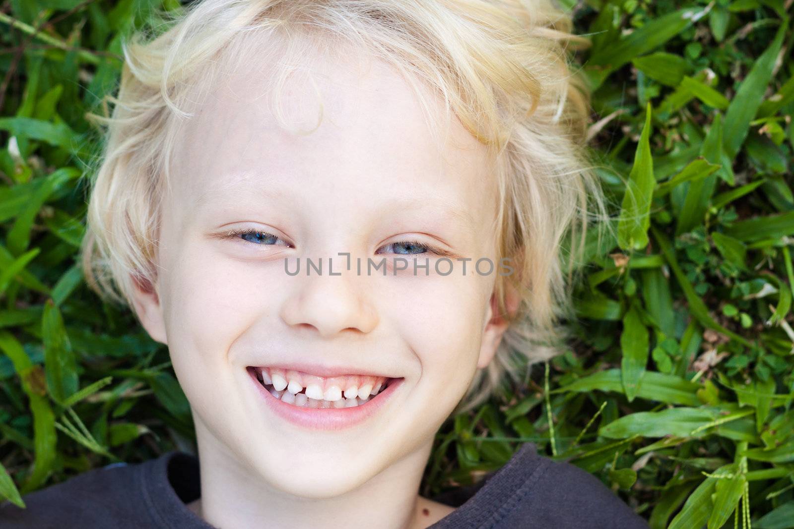 A very cute happy smiling boy lying in the grass looking at camera.