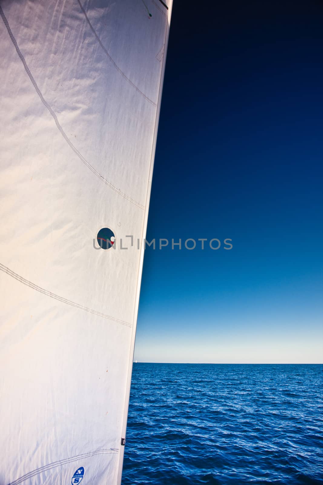 Closeup of the white sail of a sailboat and a calm blue ocean under a hot clear blue summer sky while sailing mid ocean