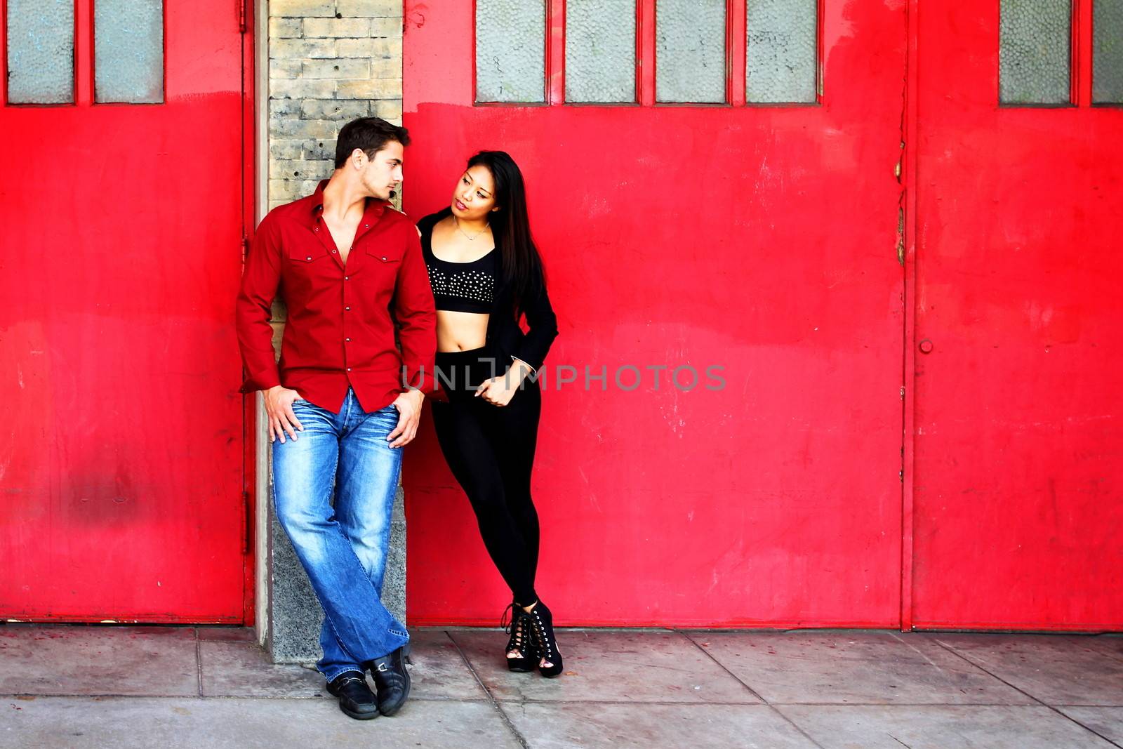 Young couple in front of red fire station doors.