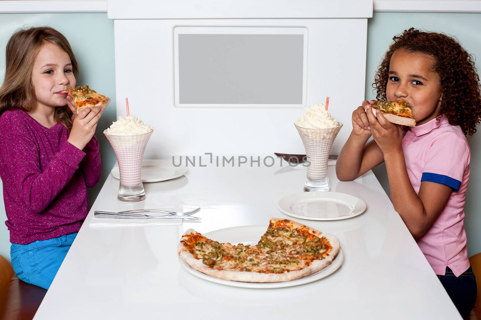 Little girls enjoying pizza in a restaurant by stockyimages