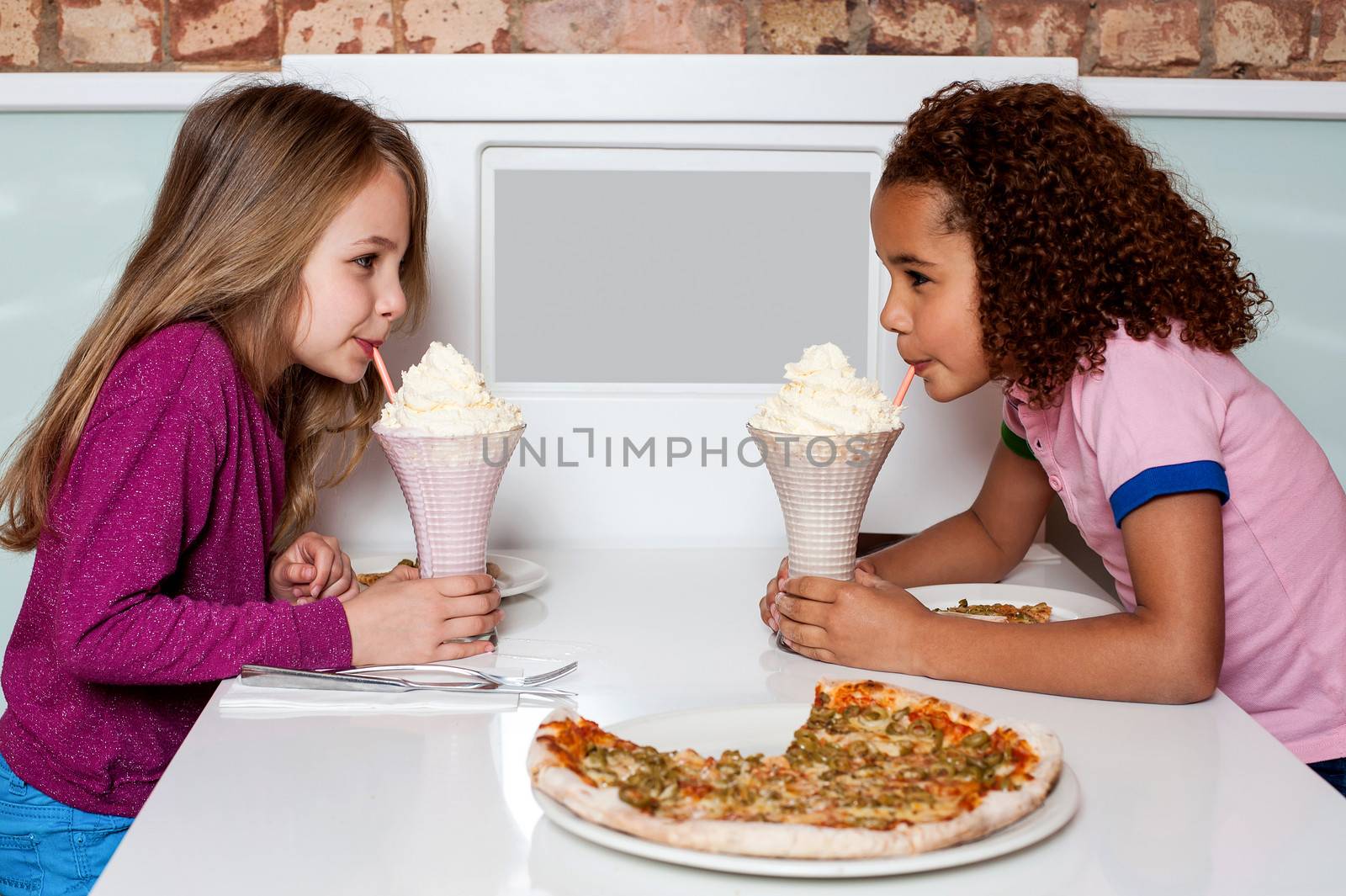 Young girls sipping strawberry shake by stockyimages
