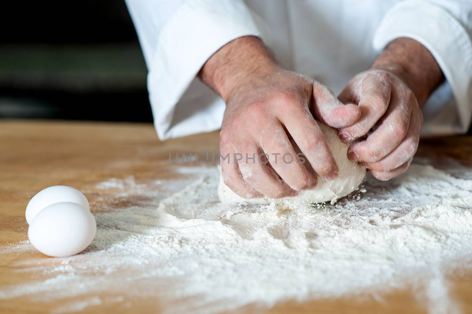 Human hands kneading dough with eggs beside