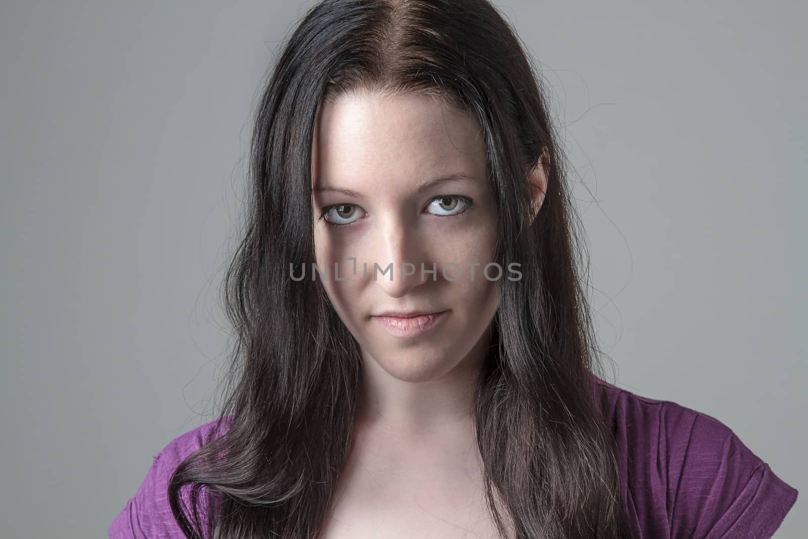 Young woman in purple shirt against a gray background, looking deeply into the camera