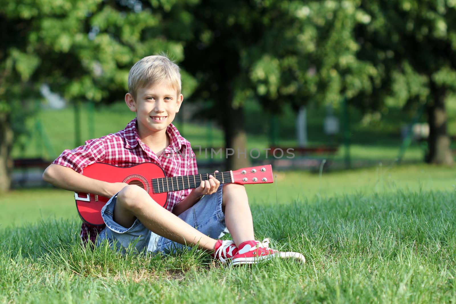 happy boy sitting on grass and play guitar by goce