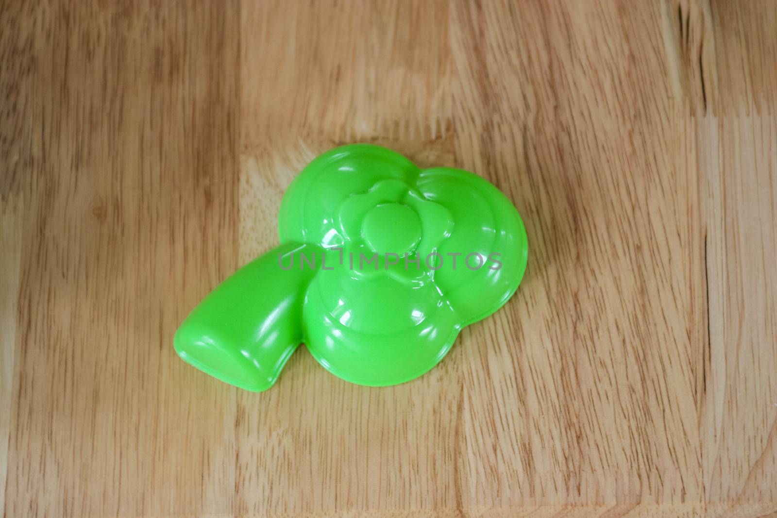 Green plastic beach toy in form of leaf on wooden background.