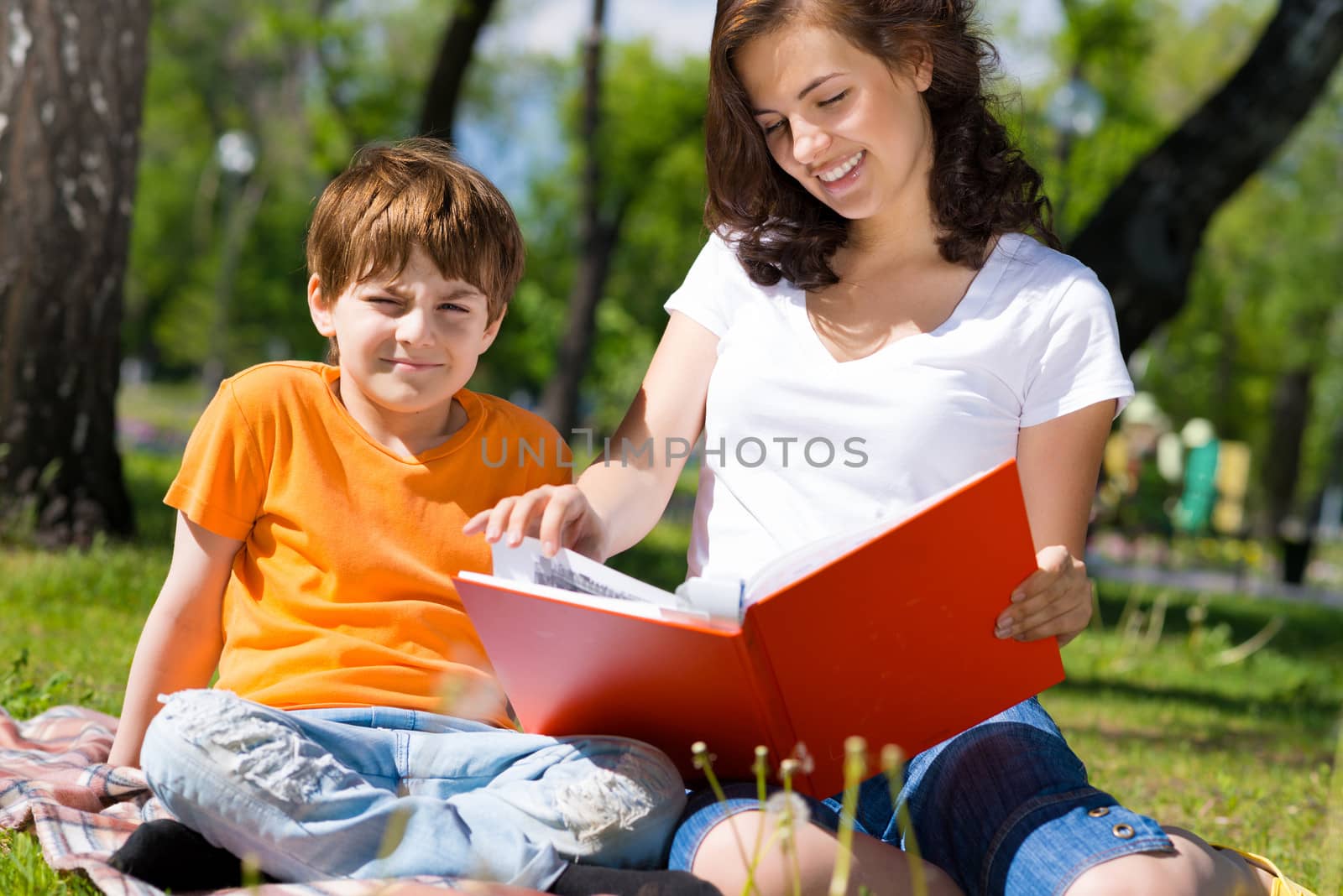 boy and a woman in a summer park reading a book together