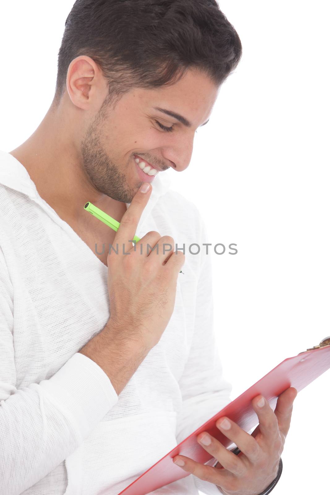 Handsome young man smiling as he reads notes on a clipboard standing with his hand to his chin, isolated on white