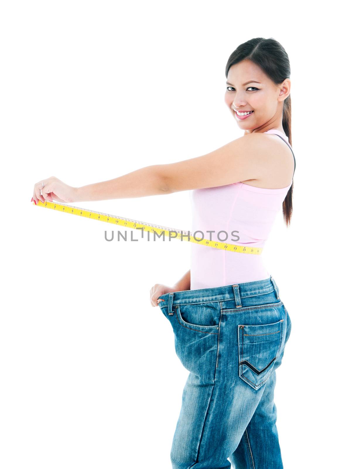Portrait of an attractive young woman measuring her waist after losing weight over white background.