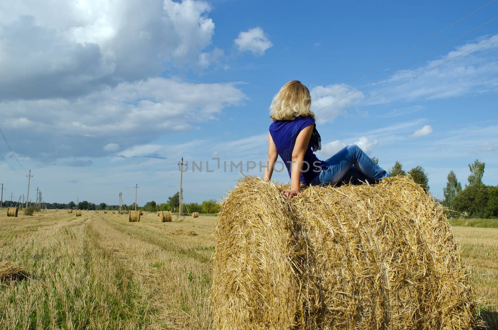 young blond girl teen sit on straw bale in agriculture field.