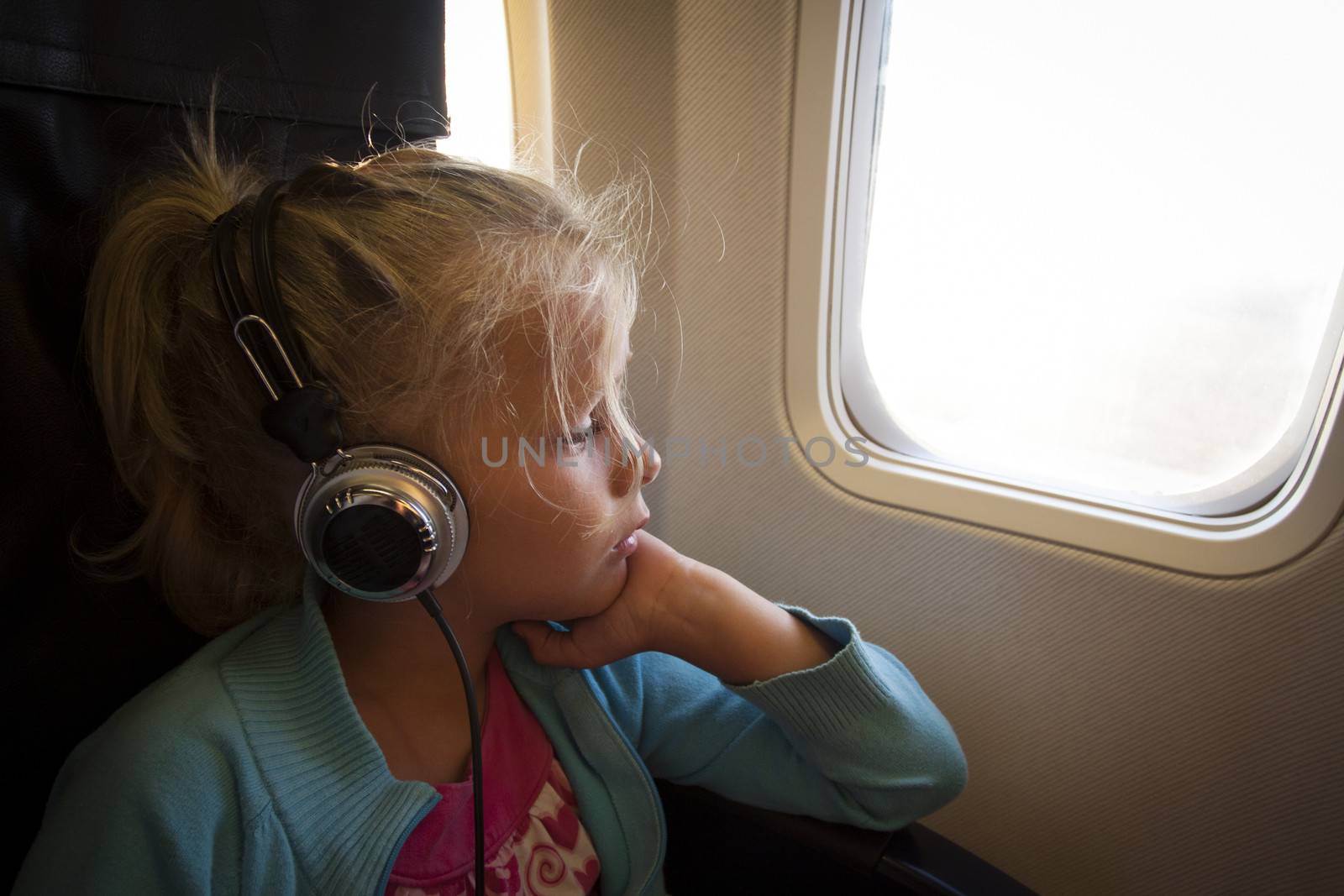 A little girl with headphones looking out of the window of an airplane