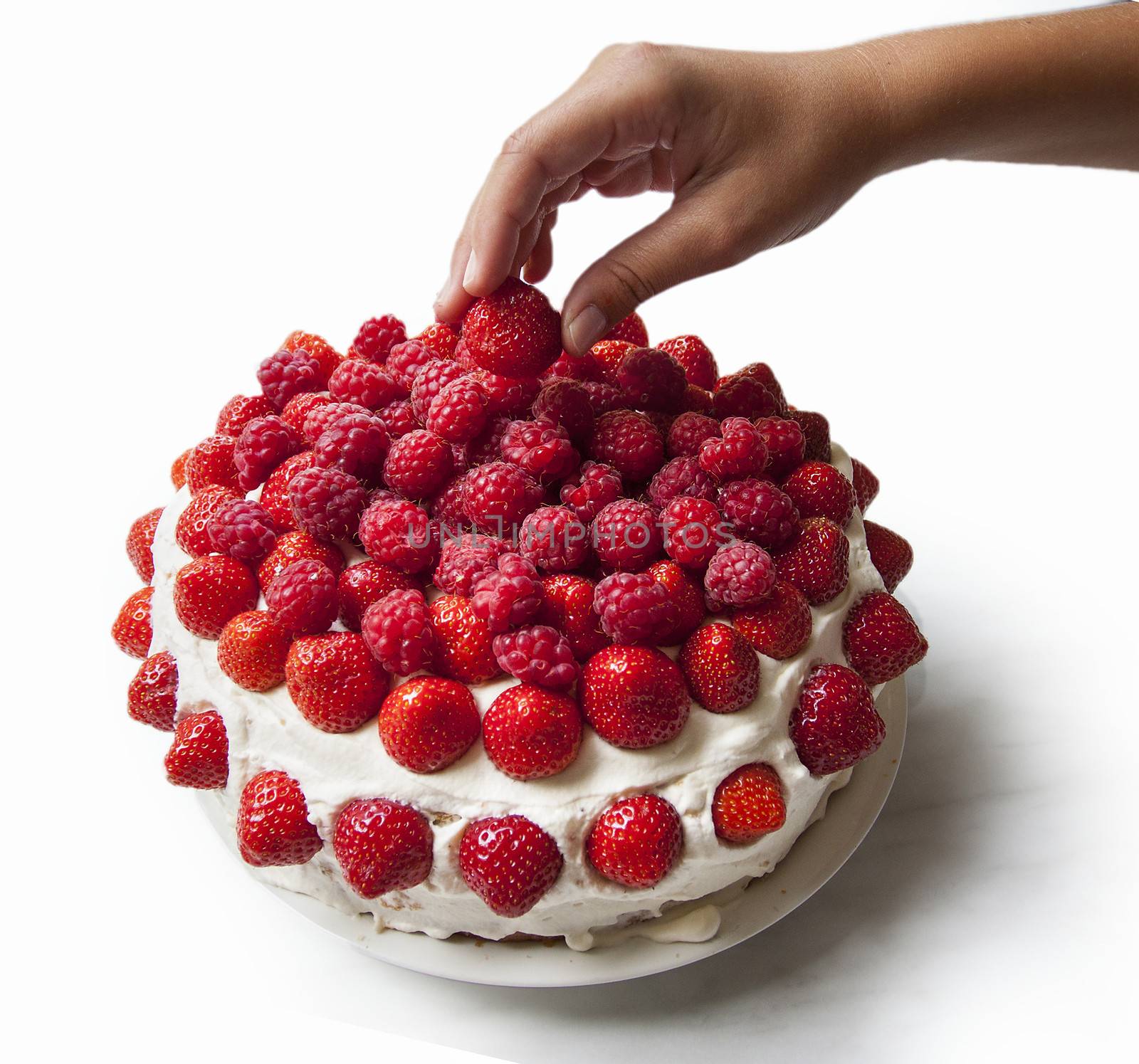 A layered sponge cake decorated with strawberries and raspberries with a hand picking of one berry. Isolated on white