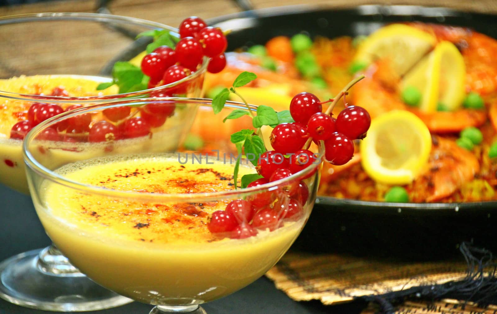 Crema catalana with red fruits and sea-food paella lunch on a menu presentation. Both are very popular dishes in the Spanish cuisine.